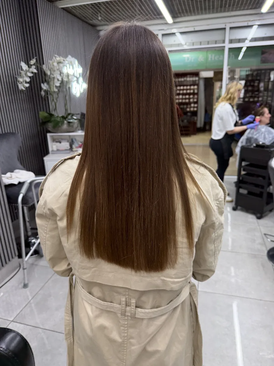 Long glossy chestnut brown hair finished in the salon, with the salon floor and retail shelving behind