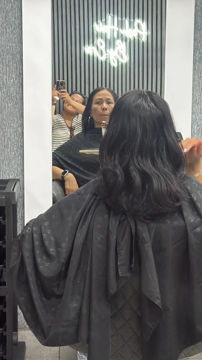 Client in a black salon gown with long dark waves, seen from behind toward the salon mirror